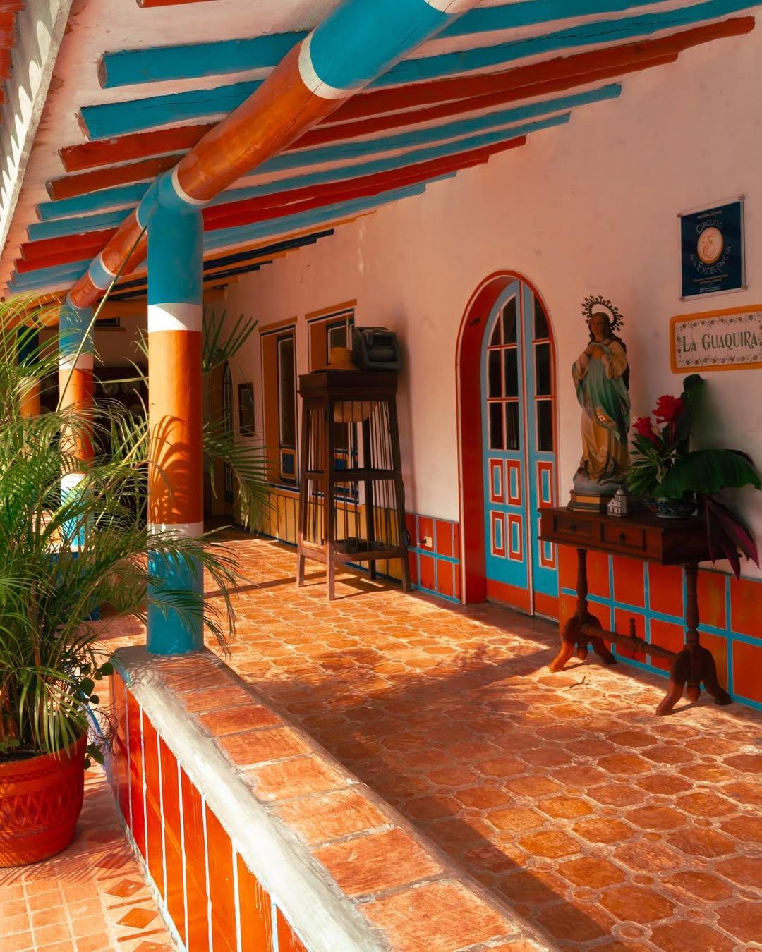 Corredor de Pueblito Guáquira con columnas y vigas de colores, piso de terracota y una imagen de la Virgen